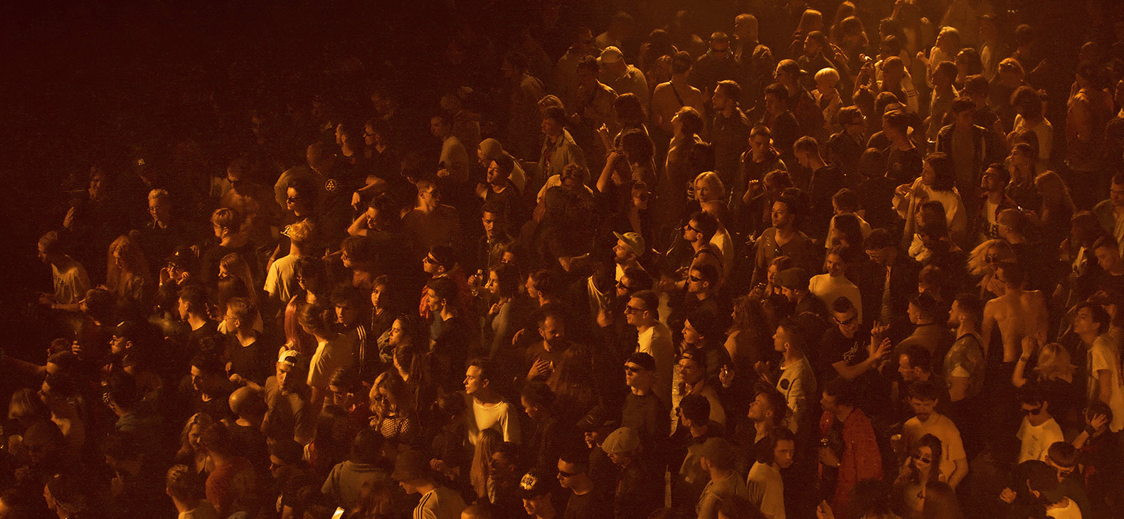 Forced Screenings: Vernissage; image: still from the video «Dedicated to the Youth of the World II» - crowd in a concert shot from above, dark atmosphere in red-yellow