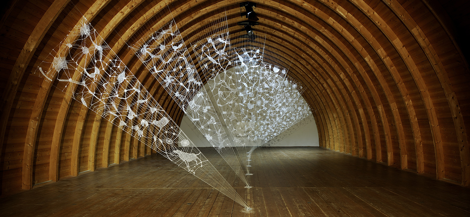 Total view of the installation by artist Zipora Rafaelov in the barrel vault of the Schafhof - European center for art of the district of Upper Bavaria. Delicate, fan-shaped installation made of 3D filament in wooden barrel vault. White motifs on seven panels stretched from the floor to the vault of the ceiling. Artist: Zipora Rafaelov; Photo: Klaus Zipa