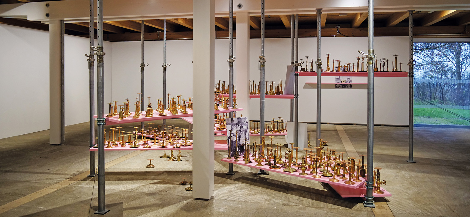 View into the exhibition; installation "Die Aufstellung" by Rebekka Bauer with several hundred metal objects on pink boards between construction supports as well as free-standing photo plates
