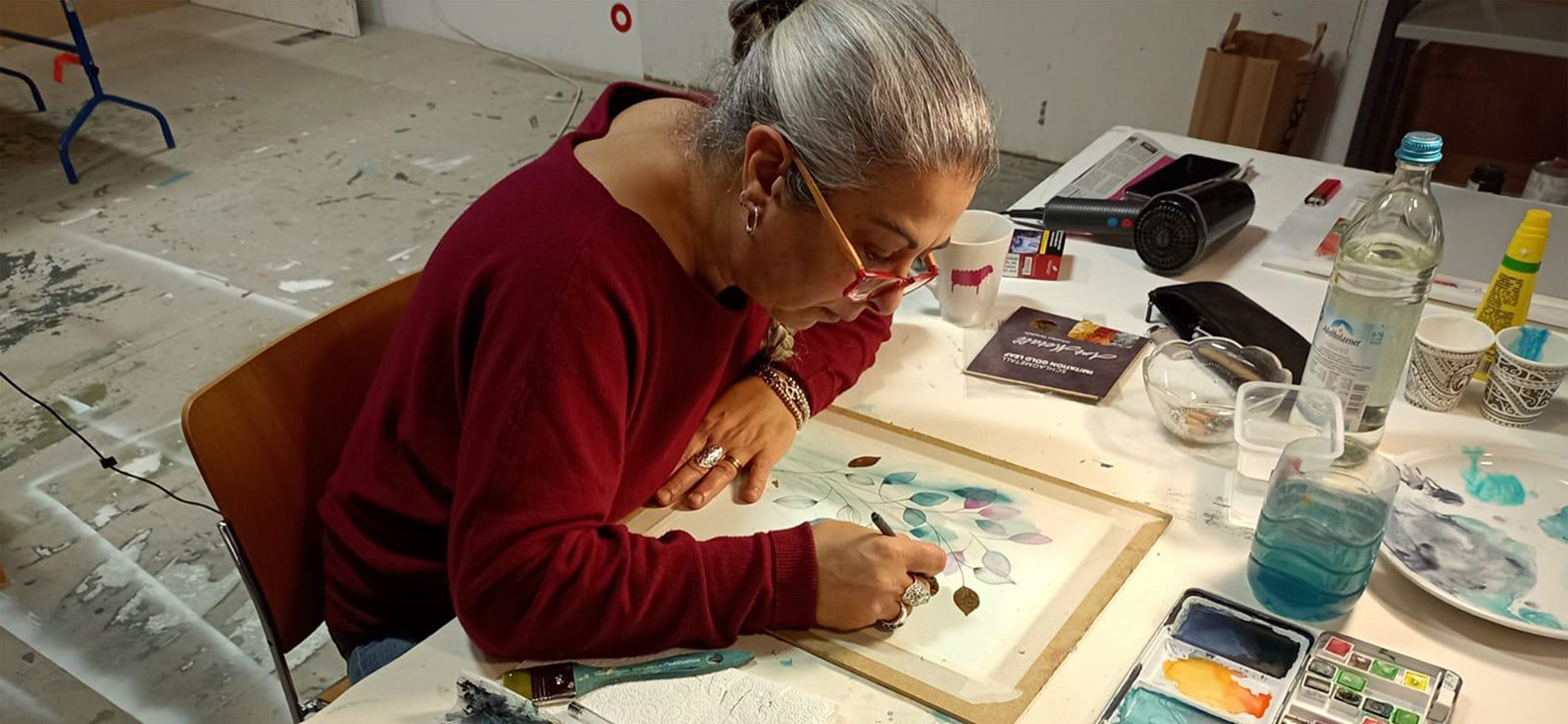 Residenzprogramm Schafhof; Künstlerinnen und Künstler 2022: Carmen Toscano. Die italienische Künstlerin Carmen Toscano ist bei der Arbeit an einem Aquarell-Gemälde zu sehen. Sie ist von schräg oben gebeugt über das Bild zu sehen.